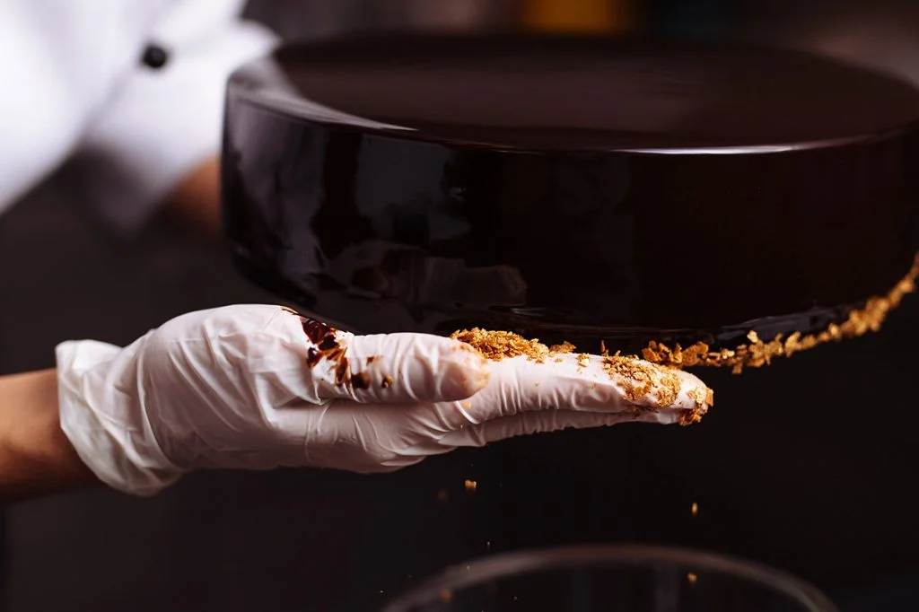 A person in white gloves is holding a chocolate cake.